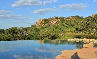 a large pool surrounded by trees and rocks with a clear blue sky in the background at Amalinda Lodge