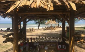 a wooden hut with a thatched roof is surrounded by trees and chairs on the beach at Ao Thai Resort
