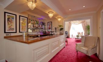 a bar with a wooden counter , wine glasses hanging from the ceiling , and a pink carpeted floor at Seacrest Hotel