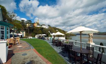 a restaurant overlooking a body of water , with several tables and chairs set up for outdoor dining at Portmeirion Village & Castell Deudraeth