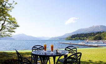 a table with two glasses of orange juice and a chair in front of a lake , mountains , and a small boat at Hakone Hotel