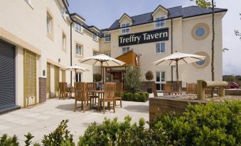 "a large outdoor dining area with several tables and chairs , umbrellas , and a sign for the "" trefry tavern "" in the background" at Premier Inn Newquay (Quintrell Downs)