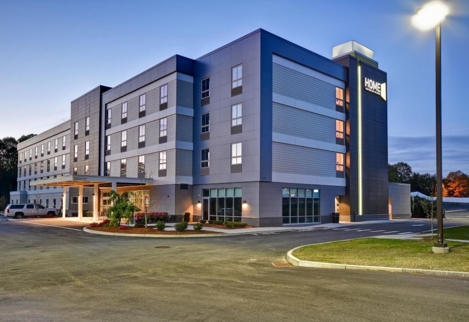 a modern hotel building with a large parking lot in front of it , under a clear blue sky at Home2 Suites by Hilton Walpole Foxboro