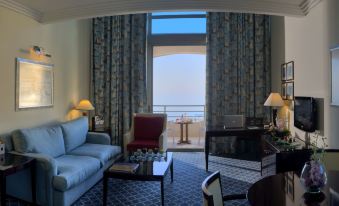 a well - furnished living room with a couch , coffee table , and dining table near a window that offers a view of the ocean at Le Royal Hotel - Beirut
