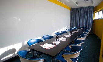 a long conference table with blue chairs and a black top is set up in a room with yellow curtains at Hotel Motel Prestige
