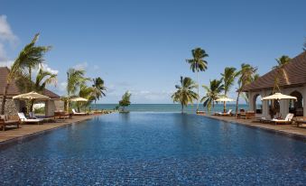 a large blue pool is surrounded by palm trees and lounge chairs with a view of the ocean at The Residence Zanzibar