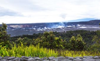 a mountainous landscape with smoke rising from the crater , surrounded by lush greenery and a stone wall at Volcano House