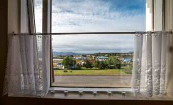 a window with white curtains offers a view of a landscape and houses in the distance at The View Apartments