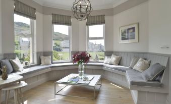 a large , empty living room with bay windows and a bench , featuring a coffee table , flowers , and a chandelier at Watersmeet Hotel