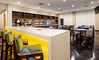 a modern restaurant with a white counter and yellow chairs , surrounded by tables and chairs at GLo Best Western DeSoto Dallas