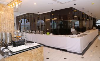 a long dining table with white tablecloths and a variety of dishes , including plates , bowls , cups , and utensils at Phoenix Hotel