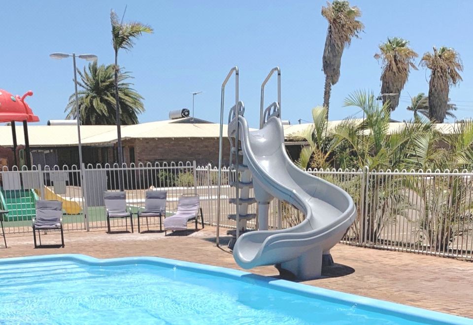 an outdoor pool with a water slide , lounge chairs , and umbrellas under a clear sky at Carnarvon Motel