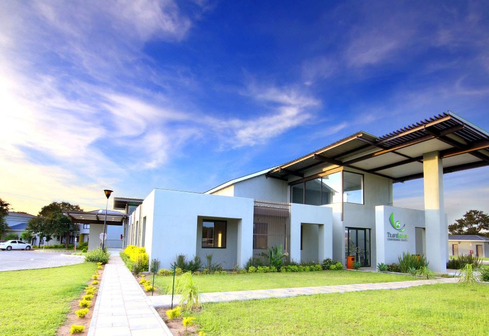 a modern white building with a green roof and large windows , surrounded by lush green grass and trees at Travelodge Kasane