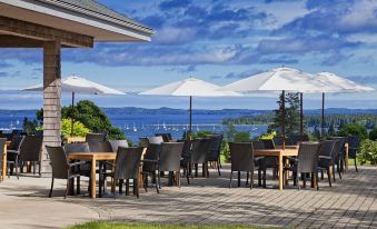 an outdoor dining area with several tables and chairs , overlooking a body of water and the ocean at The Algonquin Resort St. Andrews by-The-Sea, Autograph Collection