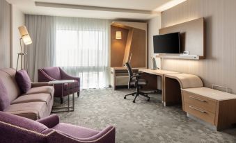 a modern hotel room with a purple armchair , desk , and window , as well as a desk with a computer monitor at Courtyard Omaha Bellevue at Beardmore Event Center
