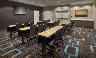 a conference room with multiple rows of tables and chairs , a large screen on the wall , and a window at Residence Inn Boston Bridgewater