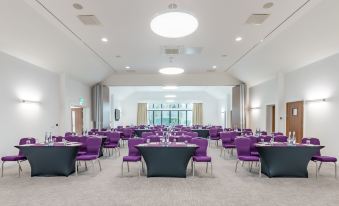 a large , empty conference room with rows of purple chairs and tables set up for a meeting or event at Aubrey Park Hotel