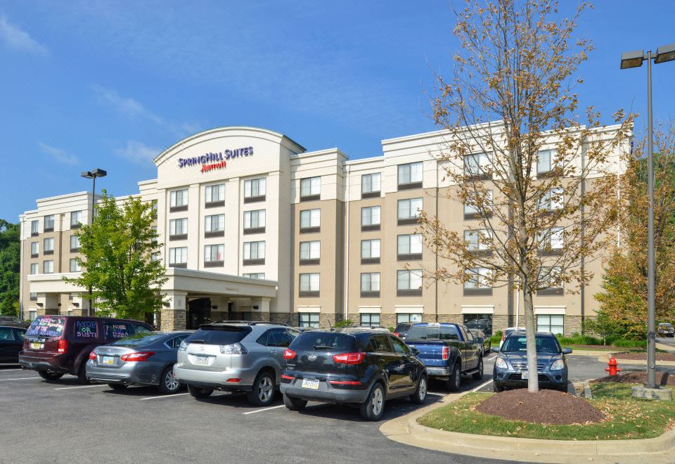 a parking lot filled with cars in front of a large hotel , with the hotel 's name displayed on the building at SpringHill Suites Pittsburgh Mills