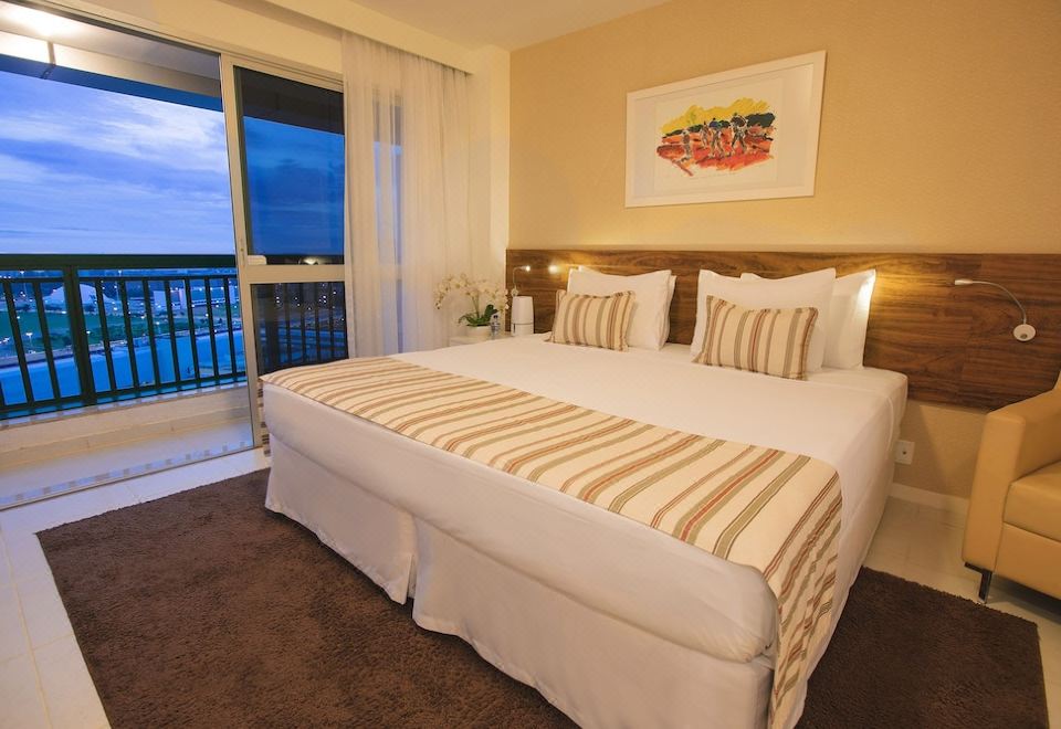 a large bed with white sheets and a striped blanket is in a room with a balcony at Hplus Vision Executive