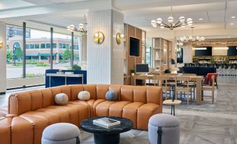 a modern living room with a brown leather couch , a black coffee table , and a dining table at Delta Hotels Muskegon Convention Center