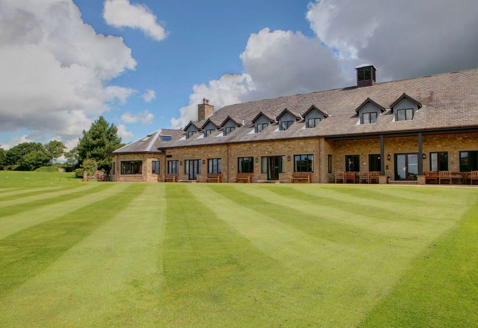 a large , stone building with a thatched roof and grassy lawns in front , under a blue sky with white clouds at Best Western Preston Garstang Country Hotel and Golf Club