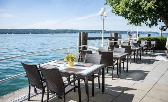 an outdoor dining area overlooking a body of water , with several tables and chairs arranged for guests at Seehotel Leoni