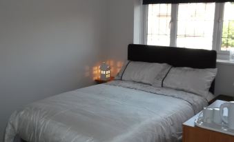 a white bed with a black headboard and two pillows , located in a room with a window at The Den