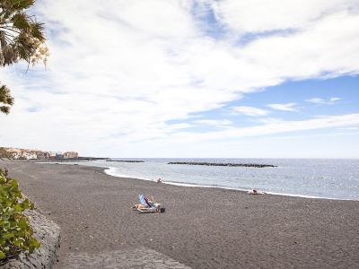 a sandy beach with a group of people sitting on lounge chairs , enjoying the view of the ocean at Lanzarote
