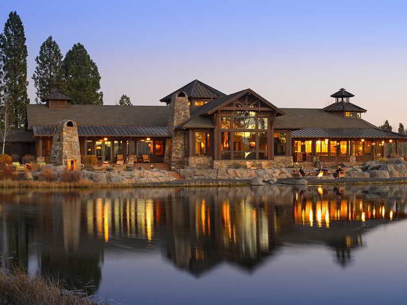 a large stone house with a thatched roof is reflected in the water , surrounded by trees at Sunriver Resort