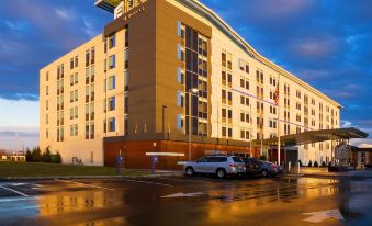 a large hotel building with a parking lot in front of it , under a cloudy sky at Aloft Mount Laurel