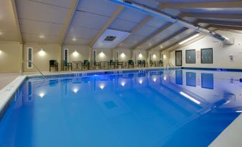 an indoor swimming pool with blue water , surrounded by chairs and tables , in a well - lit room at La Quinta Inn & Suites by Wyndham Springfield MA