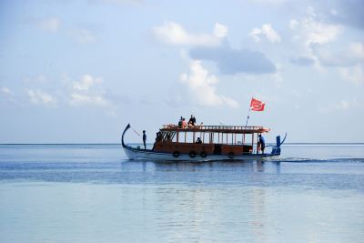 a boat with a red flag on its side is sailing in the ocean near shore at Vilamendhoo Island Resort & Spa