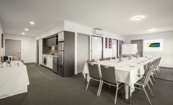 a dining room with a long dining table surrounded by chairs , and a kitchen in the background at Quest Werribee