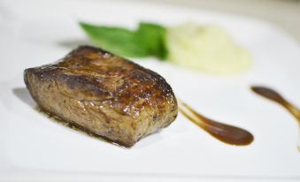 a square plate with a piece of meat on it , accompanied by a small bowl of sauce at Drake Bay Getaway Resort