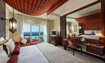 a large bedroom with a bed , desk , and chairs is shown with a view of the ocean at Ajman Hotel Managed by Blazon Hotels