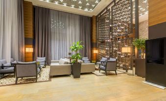 a modern hotel lobby with wooden flooring , multiple couches , chairs , and potted plants , creating a comfortable atmosphere for guests at Golden Tulip Istanbul Bayrampasa