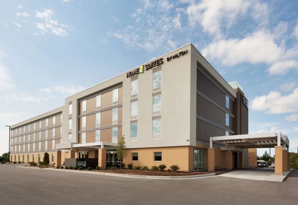 a large , modern hotel building with a large sign above the entrance , surrounded by trees and other buildings at Home2 Suites by Hilton Milwaukee Brookfield