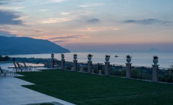 a serene view of the ocean from a grassy area with stone railings and flowers at Best Western Plus Hotel Terre di Eolo