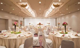 a large , well - decorated banquet hall with multiple round tables set for a formal event , including white tablecloths , pink centerpieces at Kawasaki Nikko Hotel