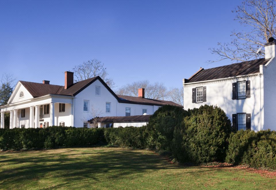 a large white house surrounded by a grassy field , with a fence surrounding the property at The Inn & Tavern at Meander