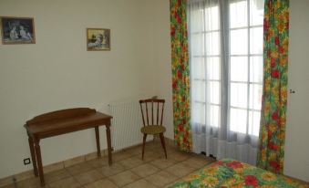a room with a wooden desk , chair , and colorful window curtains has a floral - patterned bedspread at L'Horizon