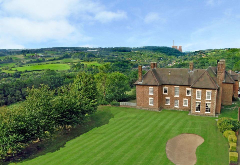 a large house is surrounded by a green lawn and trees , with a golf course in the background at The Telford Hotel, Spa & Golf Resort