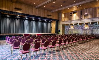 a large auditorium with rows of red chairs and a stage at the front , decorated with blue curtains at Pine Needles Lodge & Golf Club