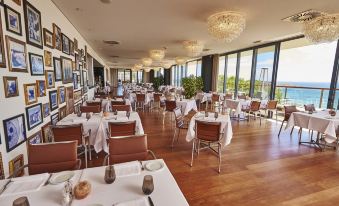 a large , empty restaurant with wooden floors and white tablecloths on tables , set for a formal dinner at Martinhal Sagres Beach Family Resort Hotel