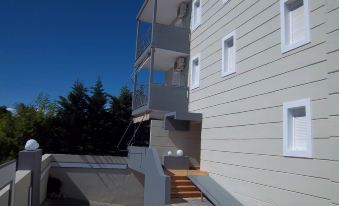 a modern building with a wooden staircase leading up to the entrance , surrounded by trees and blue sky at Milos Apartments