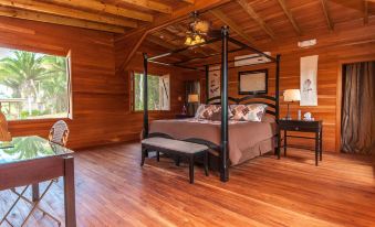 a large wooden bedroom with a four - poster bed , hardwood floors , and a large window allowing natural light to enter the room at Dream Valley Belize