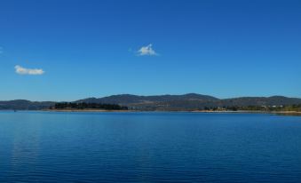 a serene lake with a clear blue sky and distant mountains , reflecting the calm water at Discovery Parks - Jindabyne