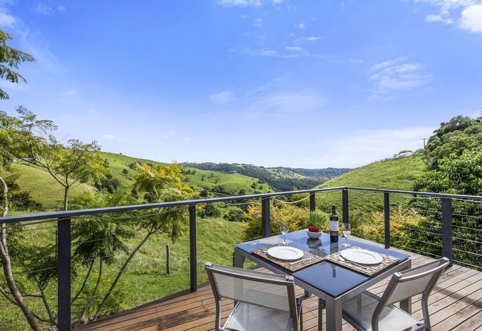 a wooden deck with a dining table and chairs , surrounded by lush greenery and a beautiful view of the countryside at Top of the Hill
