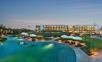 a large hotel with a pool surrounded by lounge chairs and umbrellas , set against a backdrop of trees and buildings at Royal Tulip Golf Resort Gunung Geulis