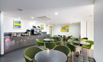 a modern , well - lit office space with green chairs and tables , a gray counter , and yellow artwork on the walls at ValueSuites Green Square